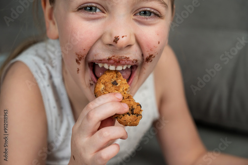 A cute little girl smeared in chocolate eats cookies while lying on the sofa.
