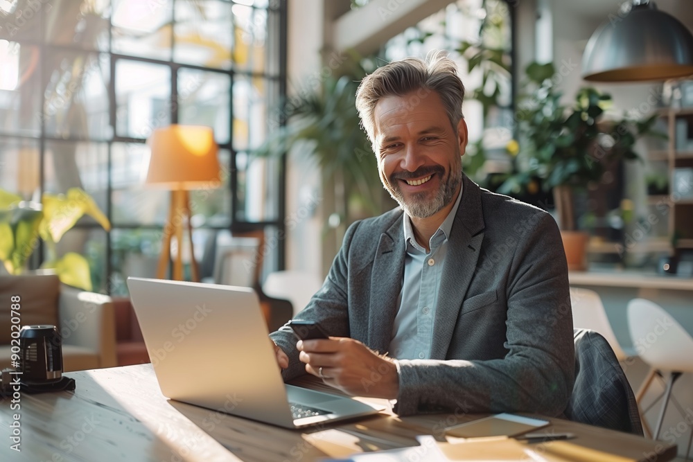 Dynamic Work Environment: Cheerful Businessman Engaged with Laptop and Phone in Sunlit Modern Office Dynamic Work Environment: Cheerful Businessman Engaged with Laptop and Phone in Sunlit Modern Office