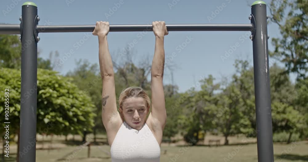 Young couple exercising in park, with a woman performing pull-ups and a man offering support on a sunny day. Young couple exercising in park, with a woman performing pull-ups and a man offering support on a sunny day.