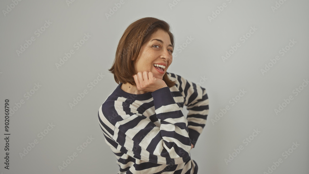 Smiling middle-aged hispanic woman in a striped sweater posing against a white wall.