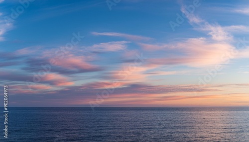 Cirrus clouds tinted pink by the sun at sunset over a calm blue ocean