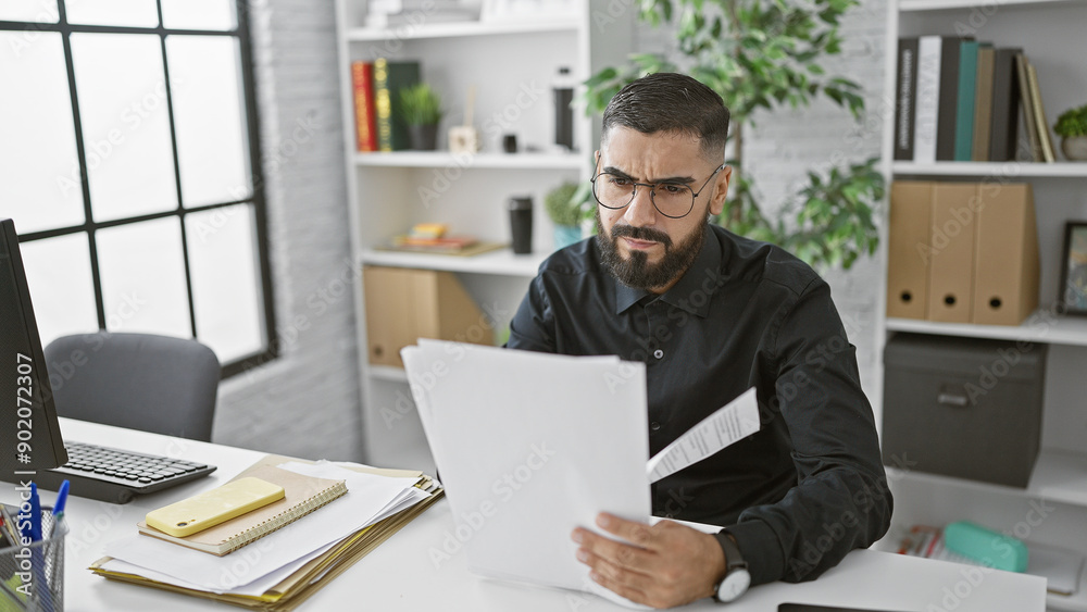 A focused bearded man reviews documents in a modern office setting with plants and bookshelves. A focused bearded man reviews documents in a modern office setting with plants and bookshelves.