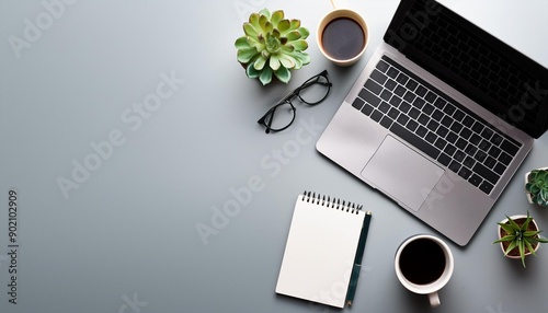 Top view of a modern workspace with laptop, plant, pencil, glasses and coffee cup.