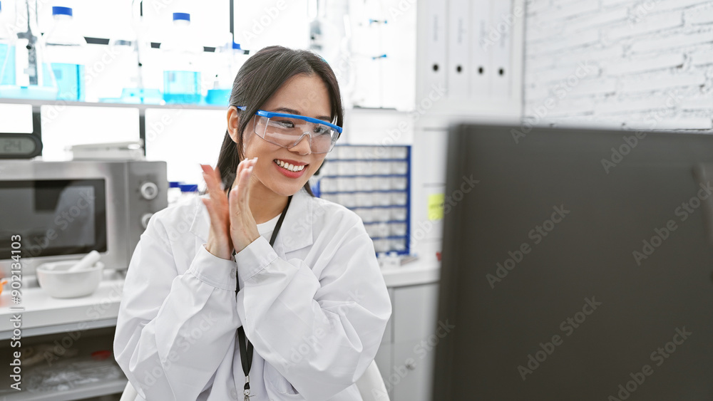 A smiling asian woman wearing lab coat and safety glasses clapping ...