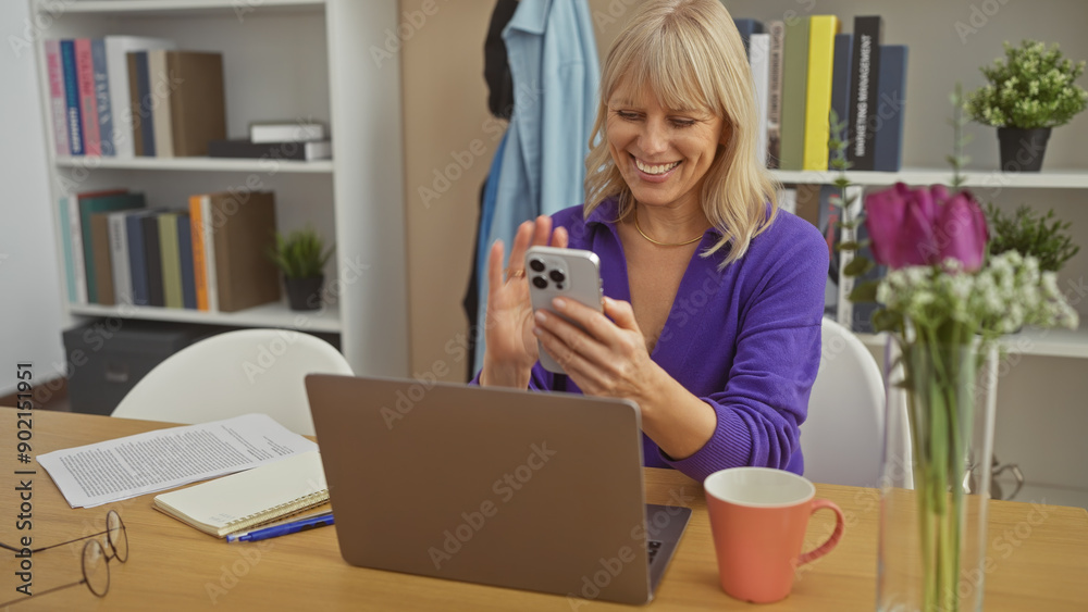 Smiling woman using smartphone at home office with laptop, flowers, and coffee mug on desk. Smiling woman using smartphone at home office with laptop, flowers, and coffee mug on desk.