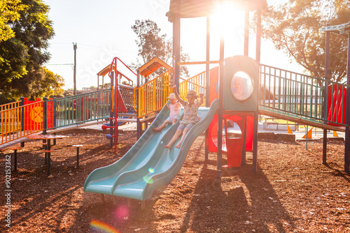 Park playground in afternoon light with children playing on slide