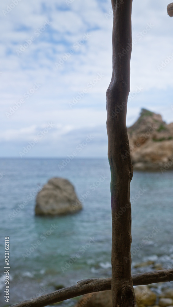 Wooden railing framing the serene coast of cala deia in mallorca with rocky outcrops under a partly cloudy sky Wooden railing framing the serene coast of cala deia in mallorca with rocky outcrops under a partly cloudy sky