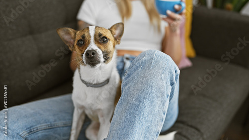 A relaxed woman holding a coffee cup with her attentive dog indoors on a couch, exemplifying companionship. photo