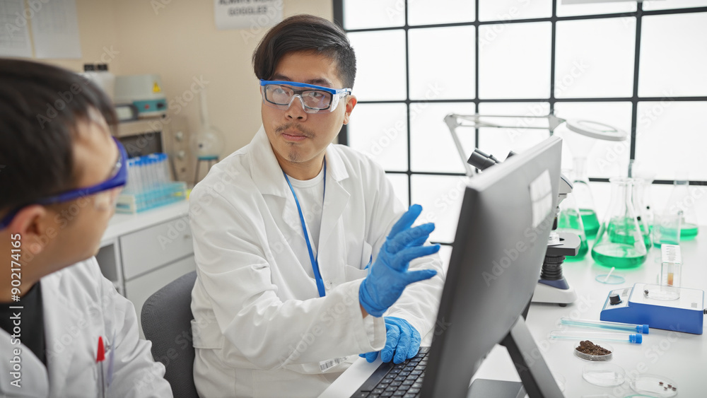 Two men in lab coats collaborate in a modern laboratory setting, using a computer among scientific equipment. Two men in lab coats collaborate in a modern laboratory setting, using a computer among scientific equipment.