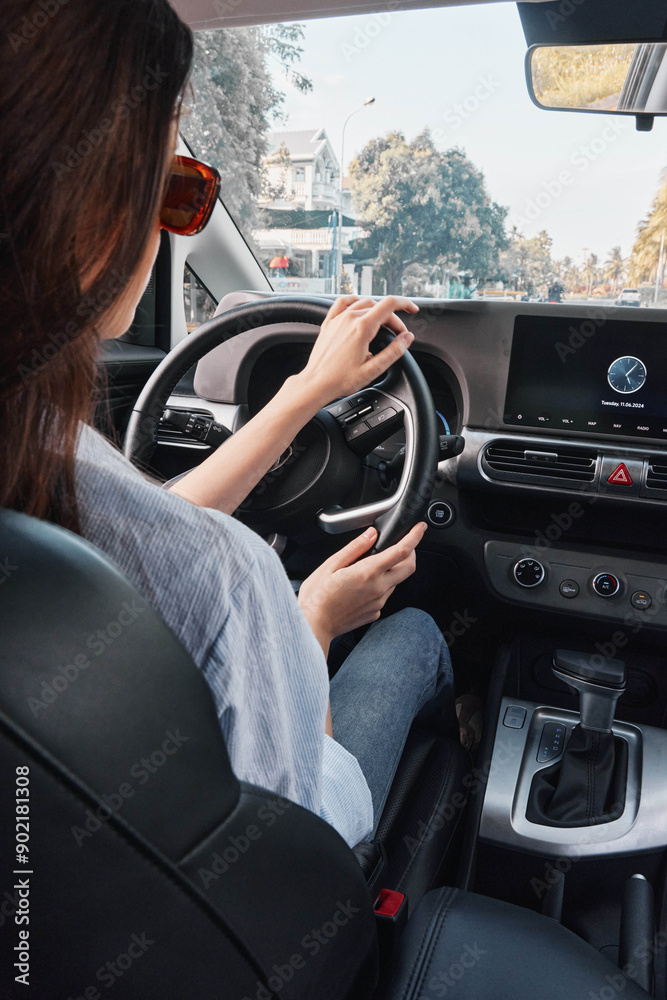 Fototapeta premium Woman driving car focuses on infotainment screen, hands on steering wheel