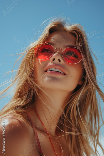 A smiling blonde woman in peach-colored sunglasses enjoying a sunny day at the beach, showcasing happiness and relaxation.