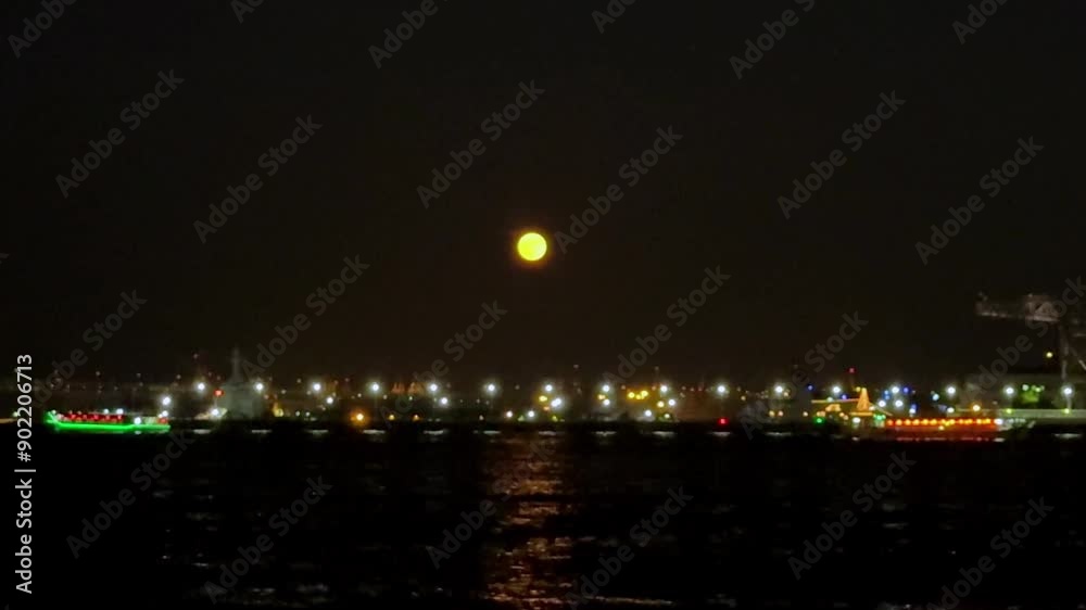 Full moon rises over a city harbor with colorful boats and sparkling lights reflecting on the water Full moon rises over a city harbor with colorful boats and sparkling lights reflecting on the water