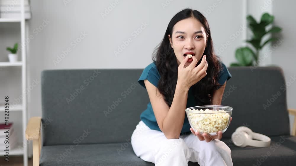Young Asian woman eats popcorn while watching TV at home. Young Asian woman eats popcorn while watching TV at home.