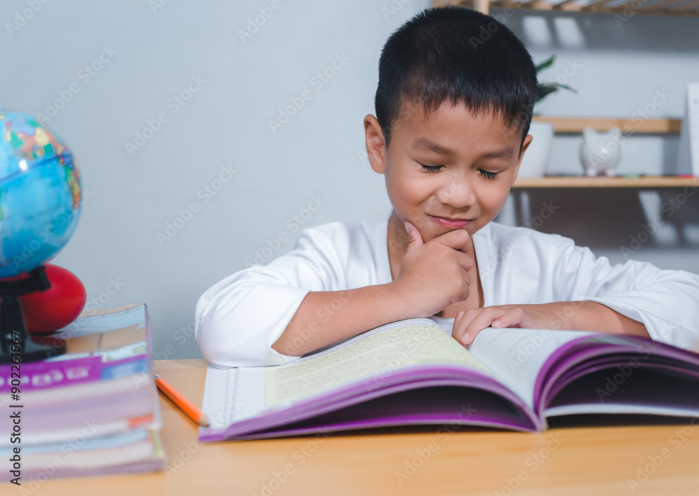 The child smile thinking sitting at table with book. Education, Childhood, People, Homework and school concept. Student learning study reading book while sitting at home. The child smile thinking sitting at table with book. Education, Childhood, People, Homework and school concept. Student learning study reading book while sitting at home.