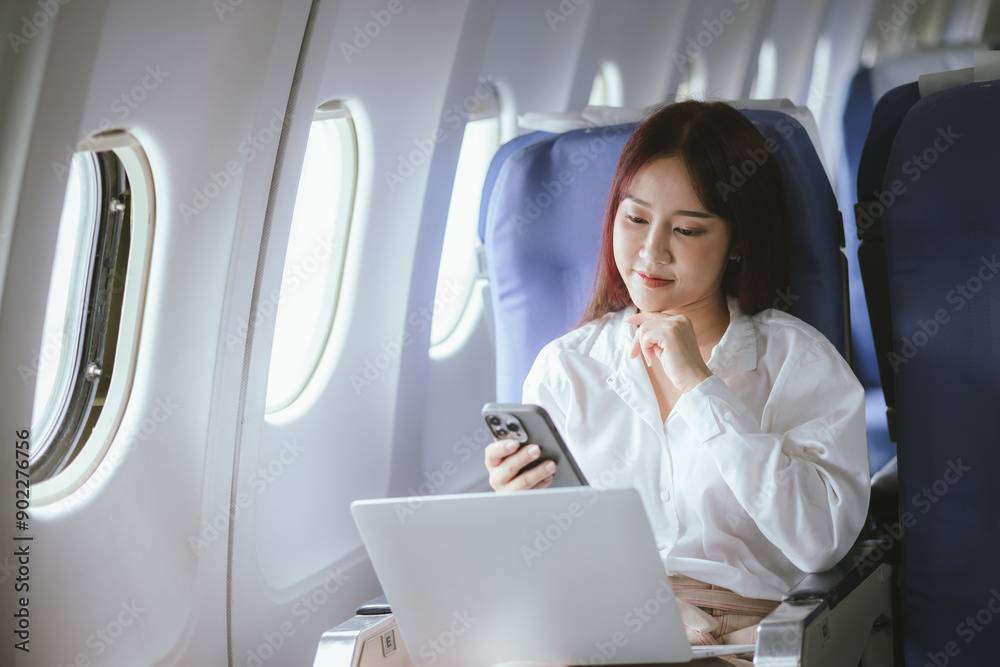 A woman sits comfortably by the airplane window, smiling as she travels. With her laptop open, she combines work and relaxation, embodying the modern lifestyle of a successful business traveler. A woman sits comfortably by the airplane window, smiling as she travels. With her laptop open, she combines work and relaxation, embodying the modern lifestyle of a successful business traveler.