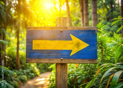 A bright yellow and blue sign with bold font and arrow shapes, mounted on a rustic wooden board, surrounded by lush greenery and morning light. photo