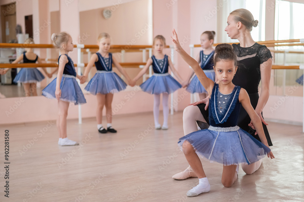 Naklejka premium Children's ballet school. Caucasian woman teaching ballet to little girls.