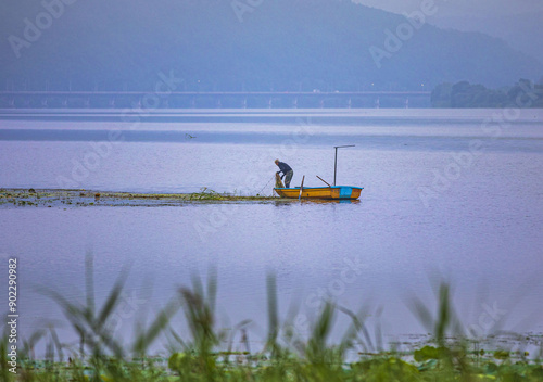 Yangsu-ri, Yangpyeong-gun, Gyeonggi-do, South Korea - July 9, 2022: Summer and morning view of a male fisherman on a ferry working with fishing net on Namhan River
 photo