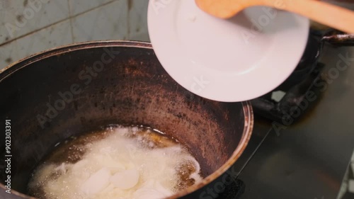 Cauldron for pilaf, cook pouring chopped onion into boiling oil with wooden spatula, preparing Uzgen pilaf, close up. photo