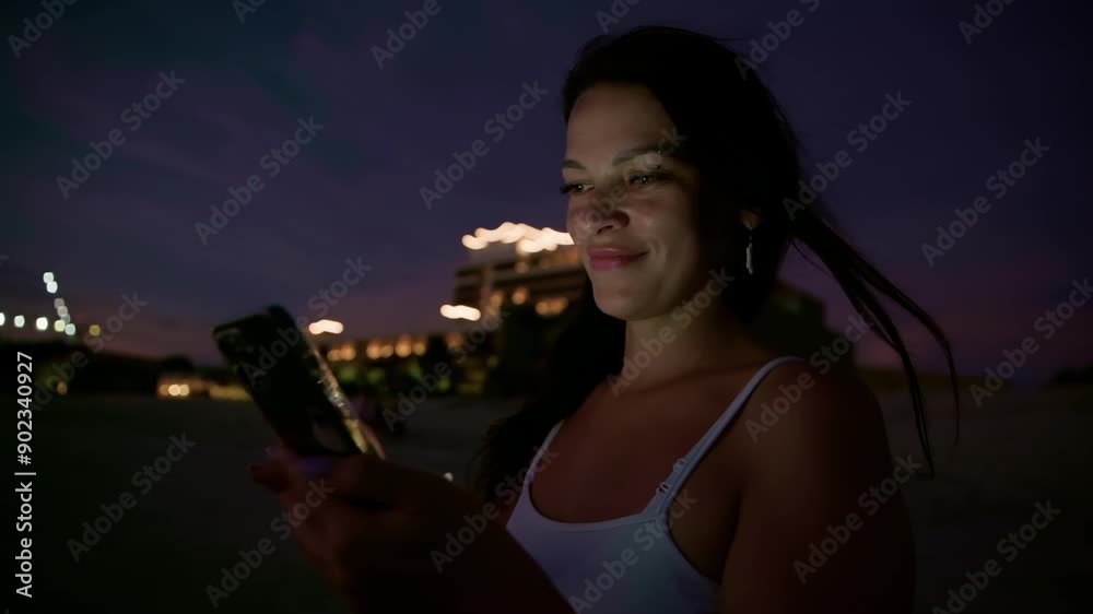 Smiling carefree woman using smartphone at night illuminated beach. Beautiful female socializing online against Illuminated resorts. She is spending leisure time during dusk. Smiling carefree woman using smartphone at night illuminated beach. Beautiful female socializing online against Illuminated resorts. She is spending leisure time during dusk.