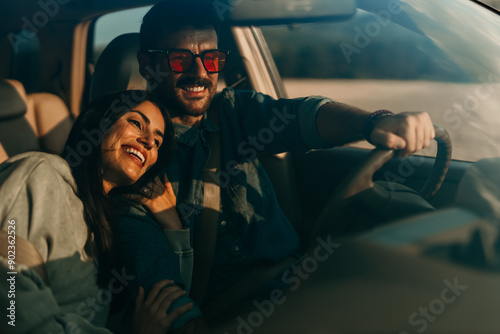 Smiling woman and man sitting in a car and enjoying driving. The woman leaned on a man's shoulder