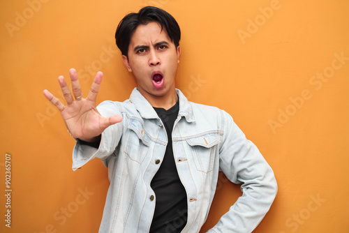 Quadro em tela Asian young man with serious face posing making stop sign with hand, Angry Asian young man doing stop gesture isolated on yellow background, defensive gesture, suitable for advertising purposes