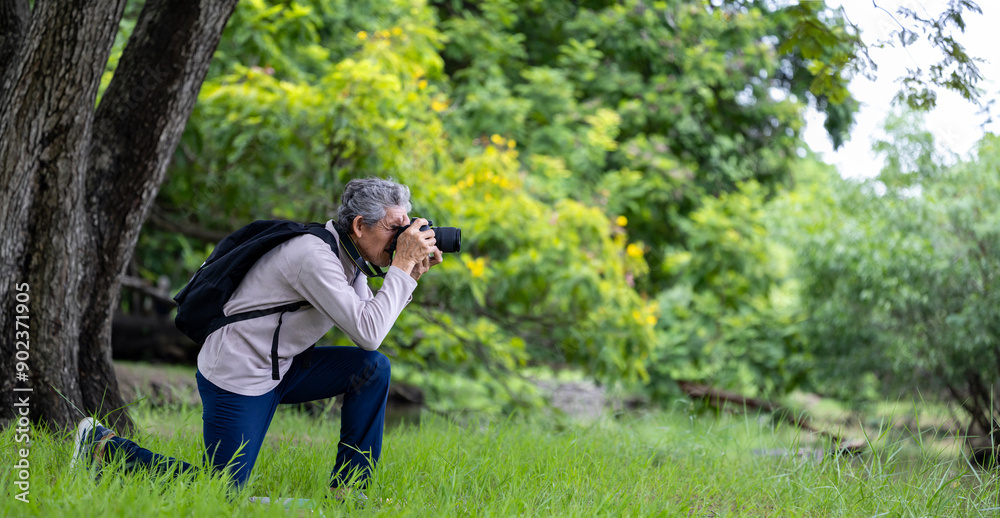 Asian senior man is trekking in the forest while using camera to take memorable photo for elder exercise outdoor and nature environment therapy Asian senior man is trekking in the forest while using camera to take memorable photo for elder exercise outdoor and nature environment therapy