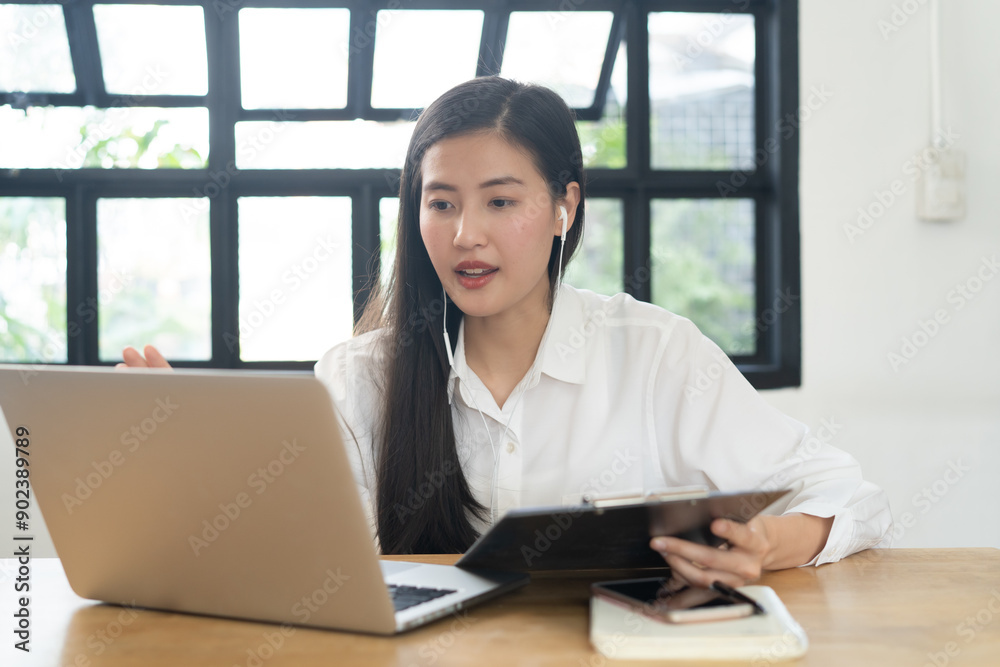 Working from home using internet communication concept. Asian young woman wear earphones talking in video conference with business partners and worker team via online internet at her home. Working from home using internet communication concept. Asian young woman wear earphones talking in video conference with business partners and worker team via online internet at her home.
