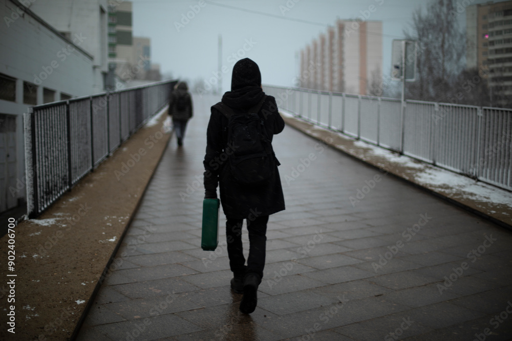 Obraz premium Guy carries suitcase down street.. Man in black clothes on cloudy day.