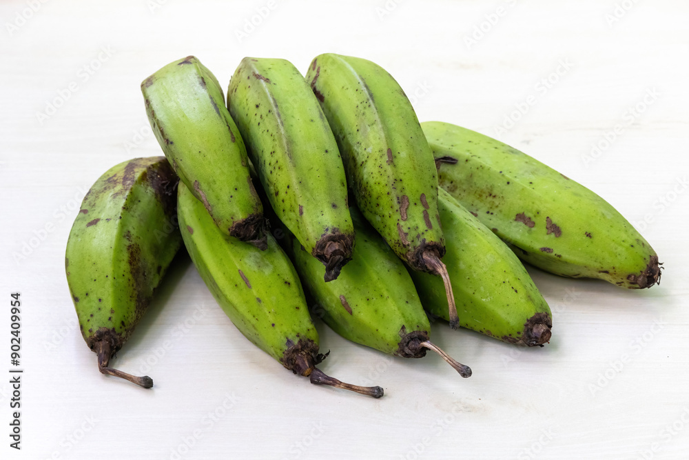 Bunch of green raw bananas on light white wooden background. Bunch of green raw bananas on light white wooden background.