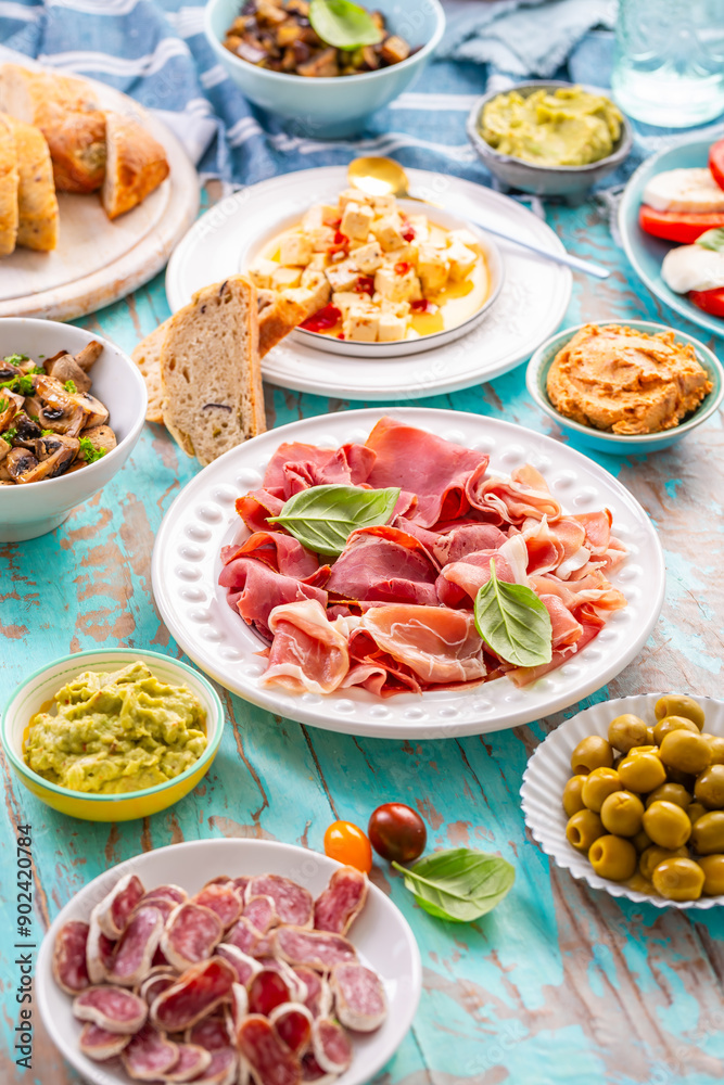 Picnic table with assorted appetizers, raw vegetables, cheese, dips, baguette and pastrami and serrano platter Picnic table with assorted appetizers, raw vegetables, cheese, dips, baguette and pastrami and serrano platter
