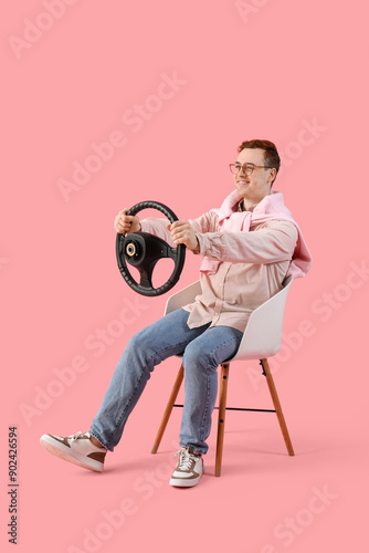 Obraz na płótnie Smiling young man driving imaginary car with steering wheel on chair, isolated o