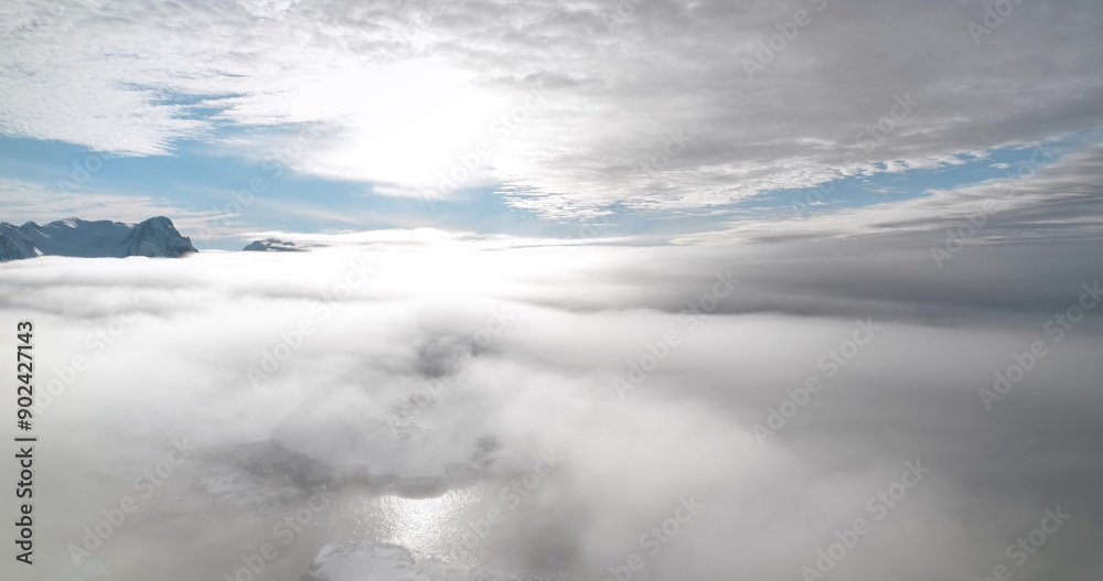 Aerial rise up flight over morning mist Antarctica coast. Majestic snow-capped mountain peaks above sunrise clouds. Fly over fog cloudscape. Ocean view surface. Wild nature background. Drone footage Aerial rise up flight over morning mist Antarctica coast. Majestic snow-capped mountain peaks above sunrise clouds. Fly over fog cloudscape. Ocean view surface. Wild nature background. Drone footage