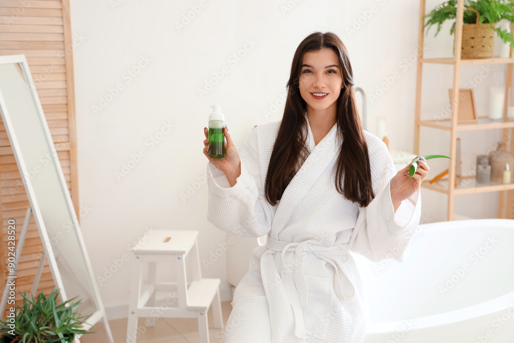 Beautiful young happy woman with aloe vera leaf and bottle of cosmetic spray in bathroom Beautiful young happy woman with aloe vera leaf and bottle of cosmetic spray in bathroom