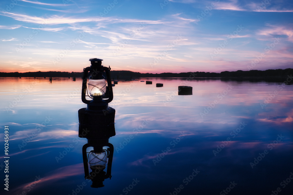 Obraz premium Sunset old Lantern over the Lake - Beautiful - Sky - Background - Lamp - Glow - Seaside - Beach - Kerosene - Lake - Burning - Vintage - Oil - Travel - Wooden - Rusty - Stake - Water - Öllampe