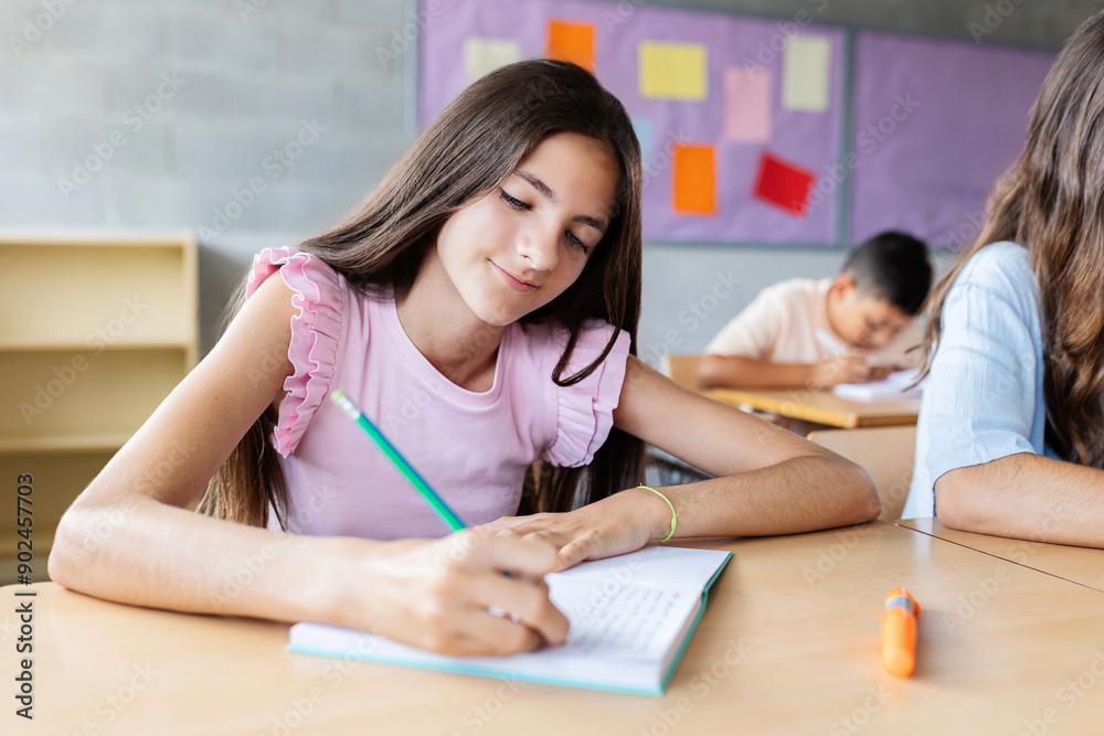 Young caucasian elementary student girl writing in notebook while studying at primary school. Children education concept. Young caucasian elementary student girl writing in notebook while studying at primary school. Children education concept.