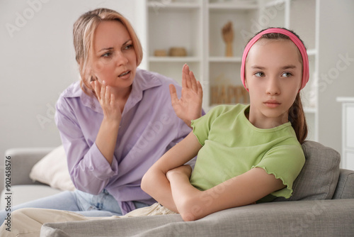 Upset teenage girl with her arguing mother sitting on sofa at home. Family difficulties concept