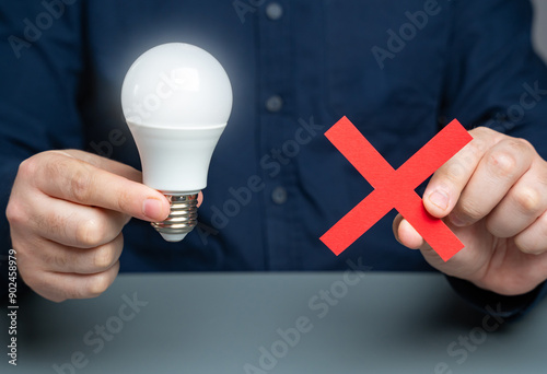 Businessman holding idea light bulb and red cross. Initiative or refusal. Removal of restrictions. Censorship of ideas and innovations. Bad idea. Disapproval. photo