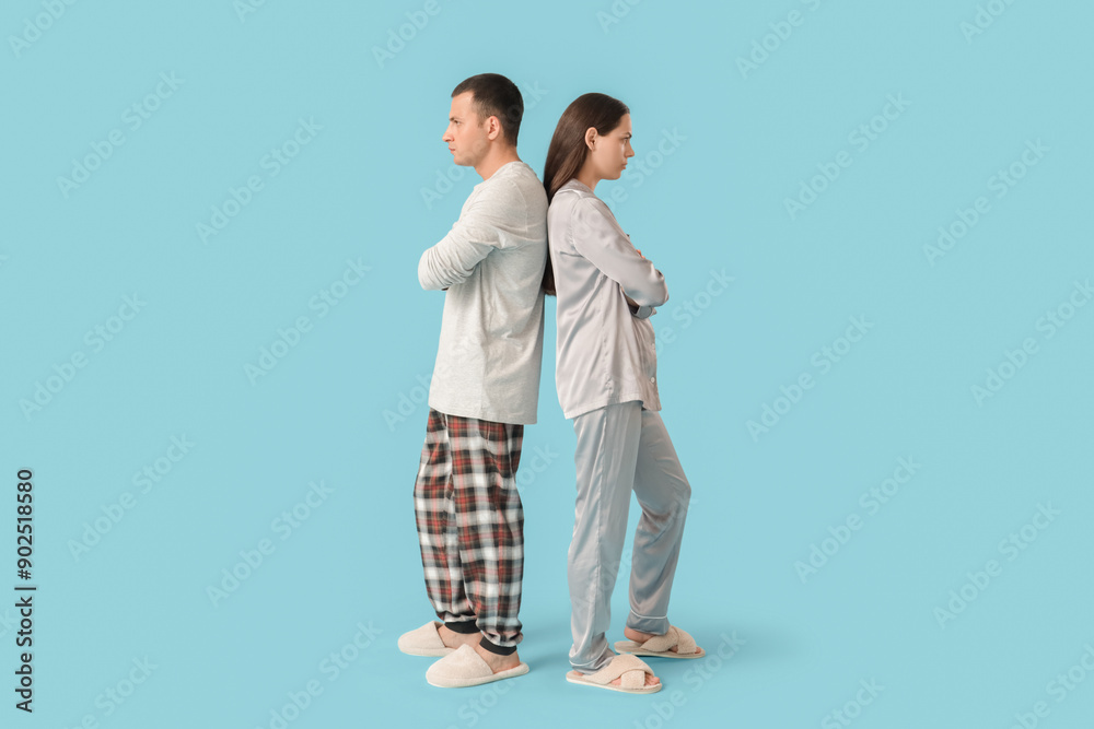Offended young couple in pajamas after quarrel on blue background Offended young couple in pajamas after quarrel on blue background