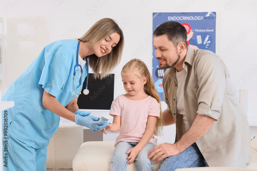 Fototapeta premium Female endocrinologist measuring blood sugar level of little girl and her father in clinic