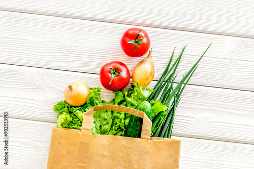 Buying fresh vegetables in paper bag on white wooden background photo