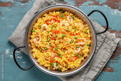 Traditional spanish seafood paella with rice, shrimps, olives and green peas in paellera on the table. Top view photo