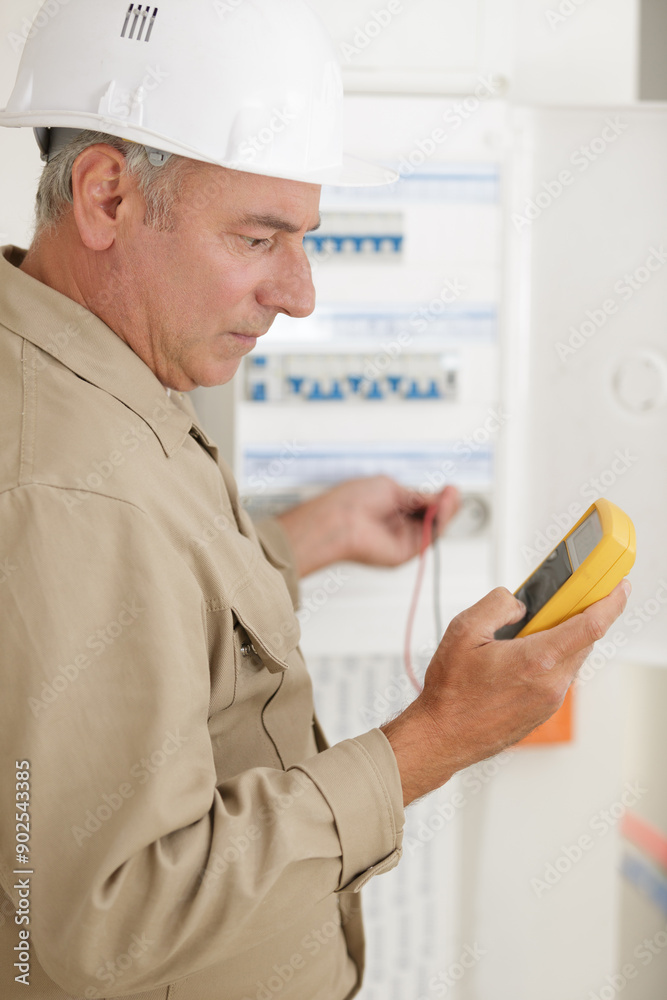 mature electrician using multimeter on circuit-breaker cabinet mature electrician using multimeter on circuit-breaker cabinet