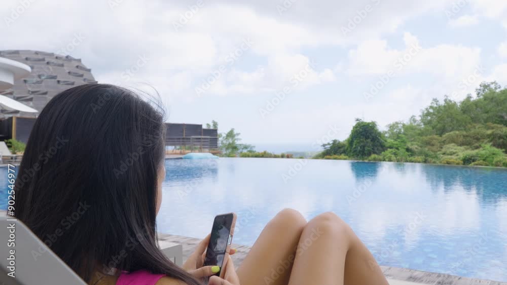 Female Guest With Smartphone Relaxing On Sun Lounger By The Poolside In Hotel. Uluwatu, Bali, Indonesia. closeup, parallax shot Female Guest With Smartphone Relaxing On Sun Lounger By The Poolside In Hotel. Uluwatu, Bali, Indonesia. closeup, parallax shot