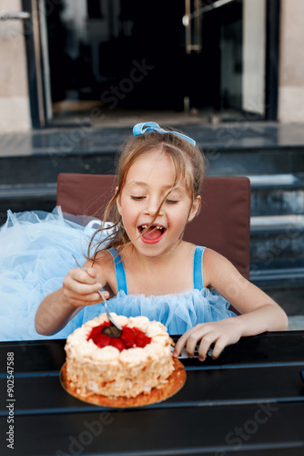Happy little girl eats birthday cake with a spoon in street cafe. Kid birthday
