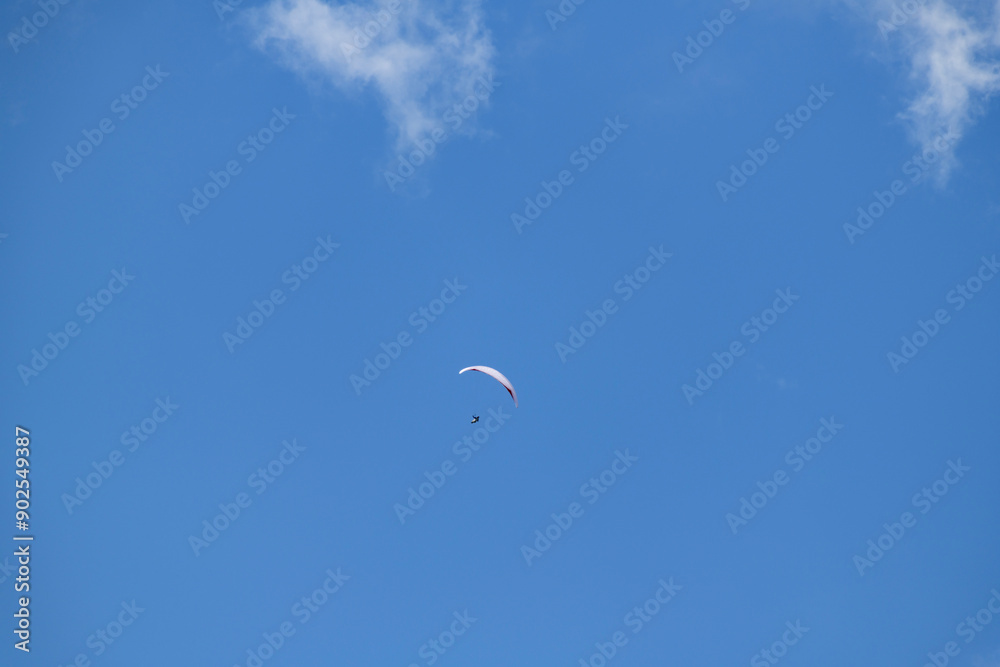 Solo paraglider flying high in a clear blue sky dotted with white clouds, epitomizing freedom and excitement Solo paraglider flying high in a clear blue sky dotted with white clouds, epitomizing freedom and excitement