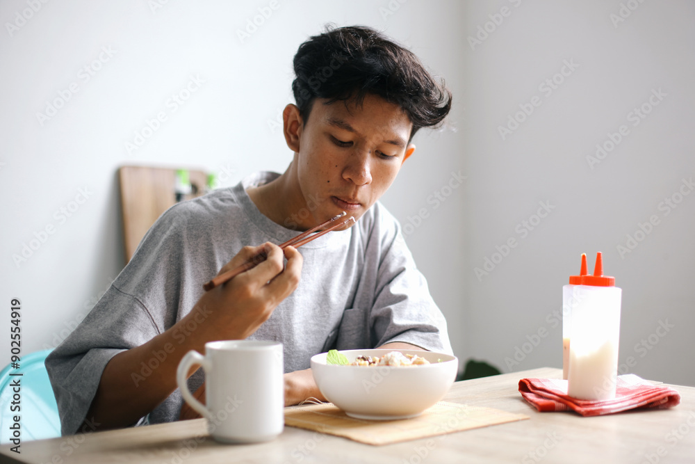 Young Asian Man enjoying Eating Salad Using Chopsticks At Home Young Asian Man enjoying Eating Salad Using Chopsticks At Home