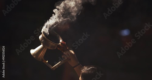 Varanasi, Uttar Pradesh, India. Man makes movements with a cup with smoking incense on the Ganga Maha Aarti ceremony. Brahman priest wearing red and yellow dress doing traditional ganga aarti at ghat