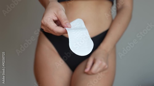 Young woman in a black panties giving hygienic daily padding for menstruation on a dark grey background. Means of women's personal hygiene during the period