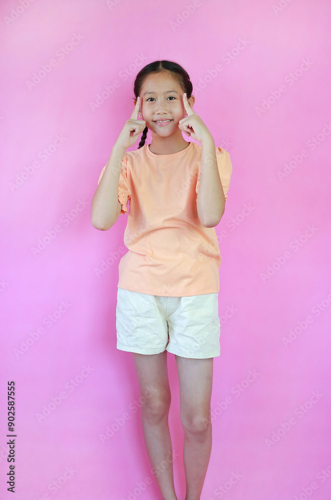 Smiling Asian young girl kid think for new idea gesture with index finger point brain head isolated on pink studio background. Smiling Asian young girl kid think for new idea gesture with index finger point brain head isolated on pink studio background.